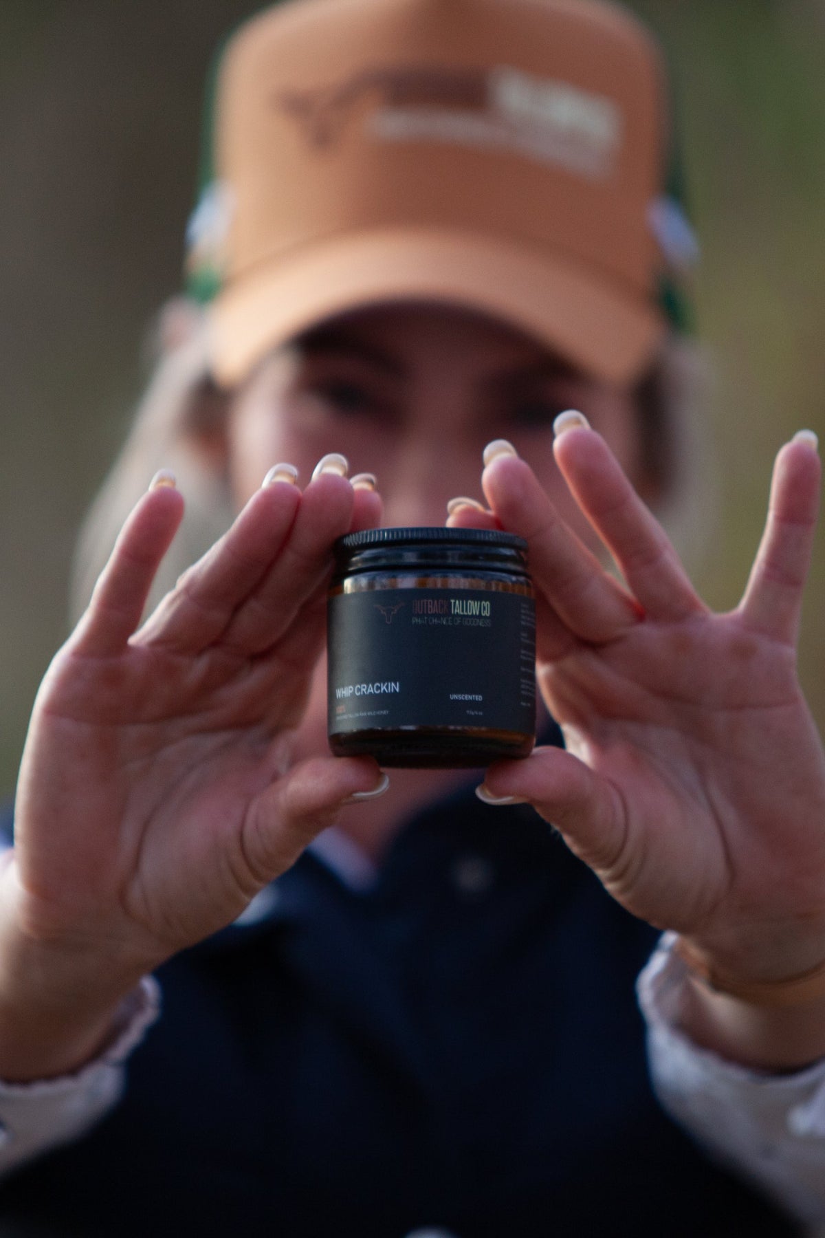 Kylie, founder of Outback Tallow Co, holding up a jar of beef tallow balm in her cap