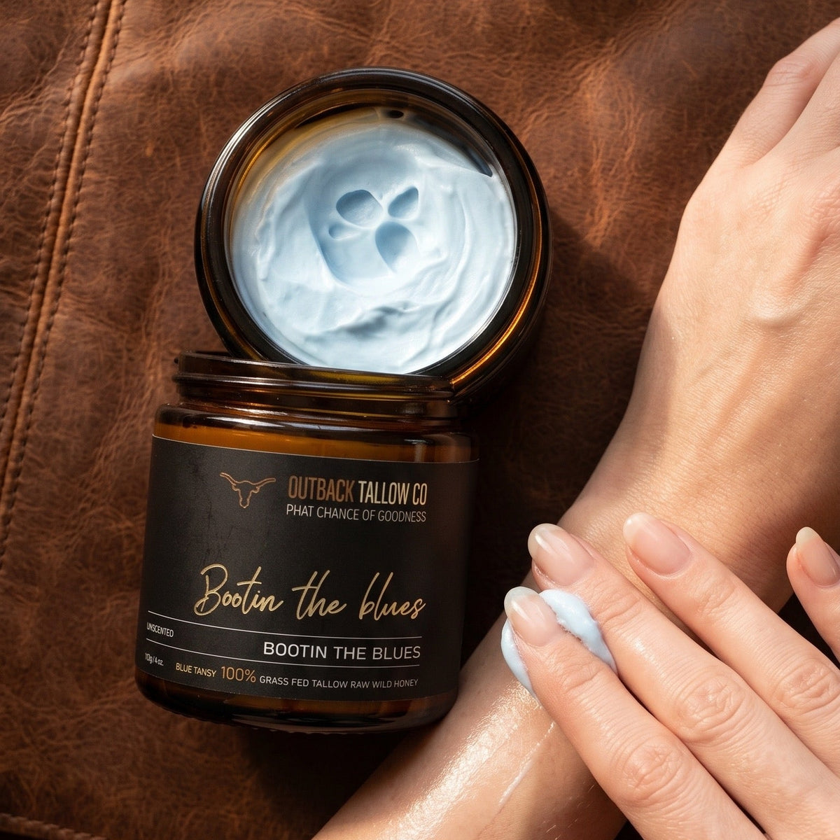 Bootin the Blues whipped grass-fed beef tallow balm for sensitive skin eczema psoriasis and rosacea open jar on rich leather background with hand applying balm natural Australian skincare no synthetic fragrance fast shipping Australia wide – Outback Tallow Co Townsville Queensland Australia