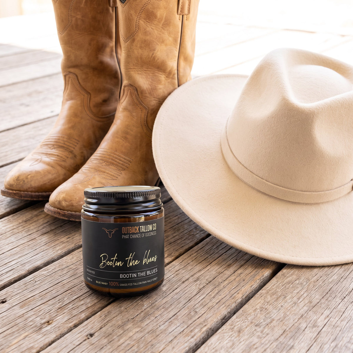 Bootin' the Blues jar on timber boards beside tan cowboy boots and a felt hat (AI-generated image)