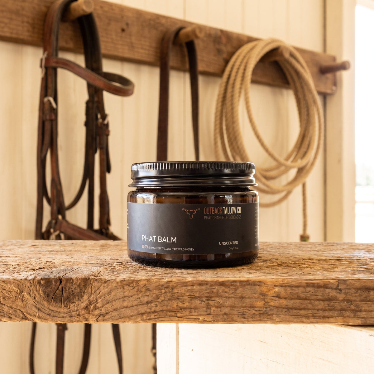 PHAT Balm jar on a tack room bench with bridles and a coiled rope (AI-generated image)