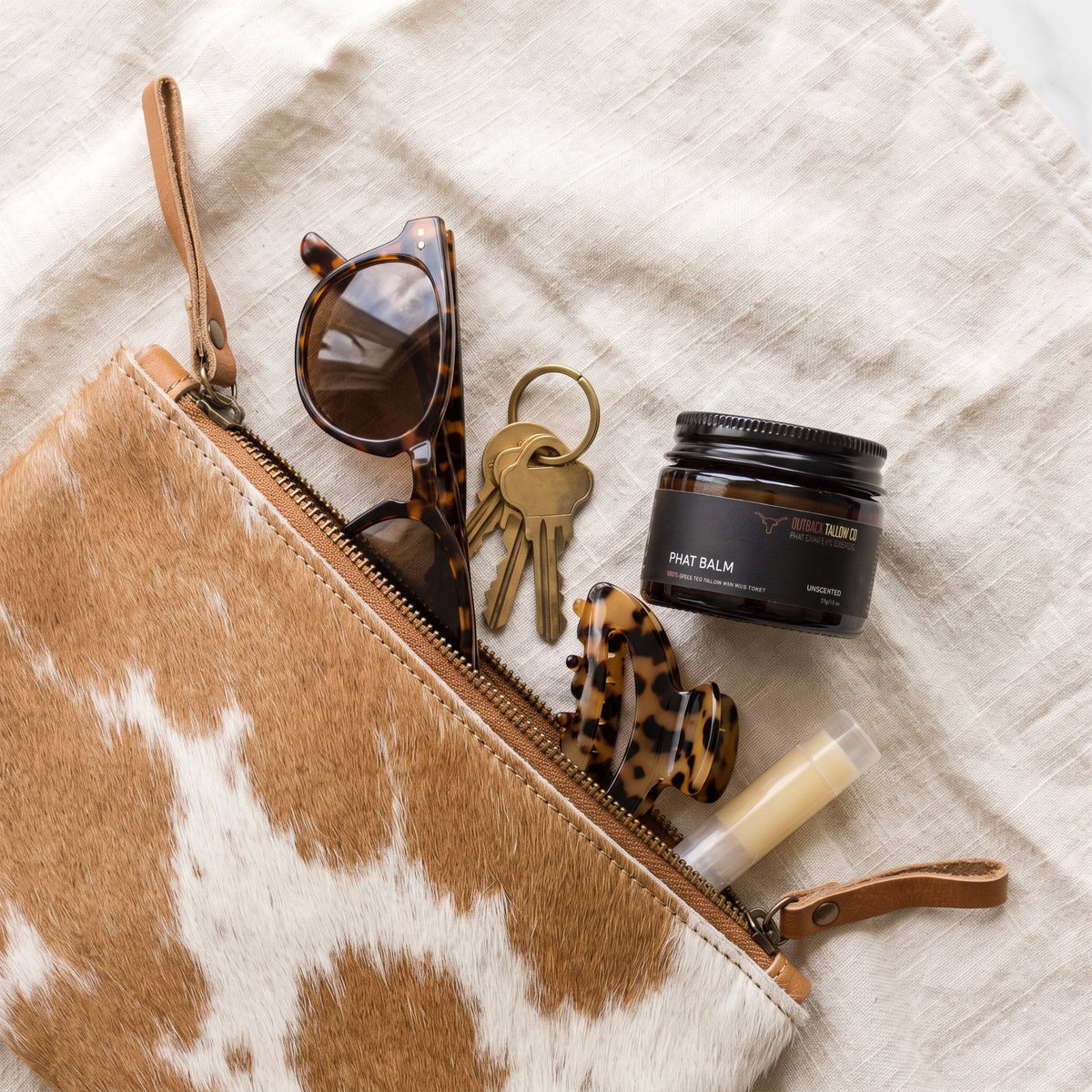 PHAT Balm 37g tallow balm jar with a cowhide clutch, sunglasses and keys (AI-generated image)
