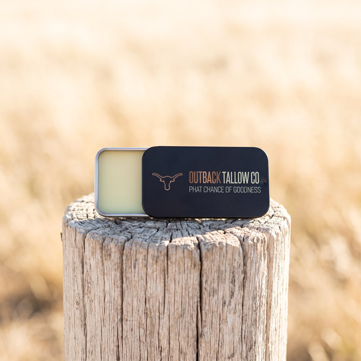 The OG tallow balm slide tin on a weathered fence post in a dry paddock (AI-generated image)