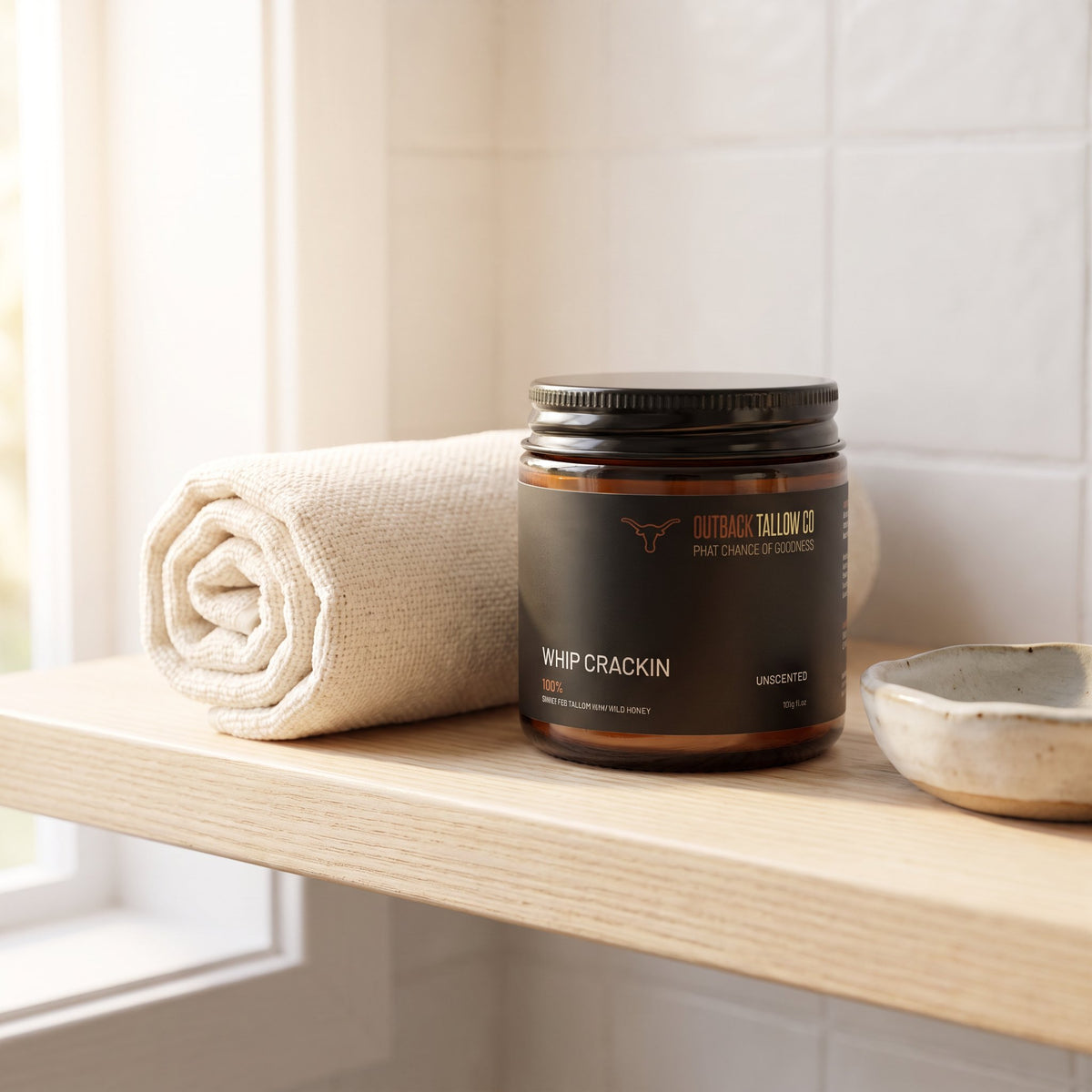 Whip Crackin' whipped body moisturiser jar on a bathroom shelf beside a rolled towel (AI-generated image)